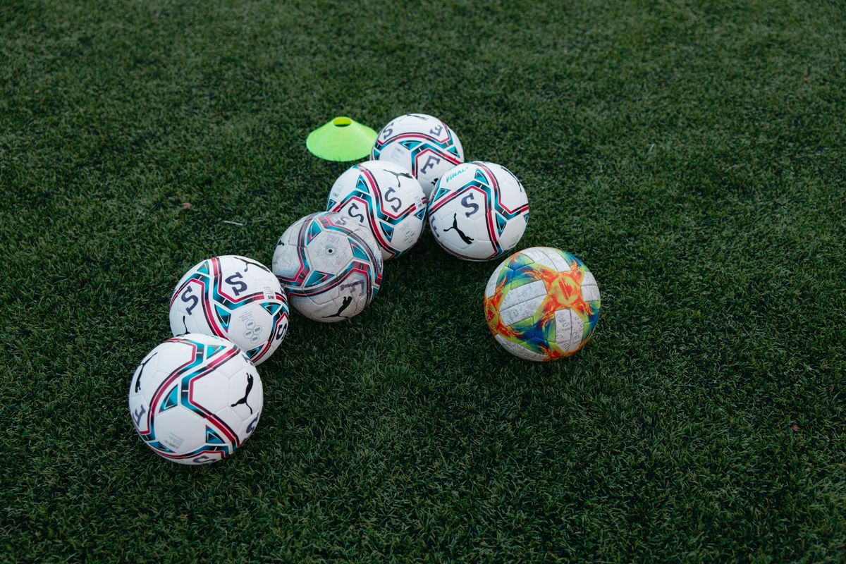 Several footballs with blue and red patterns arranged on a grass training field