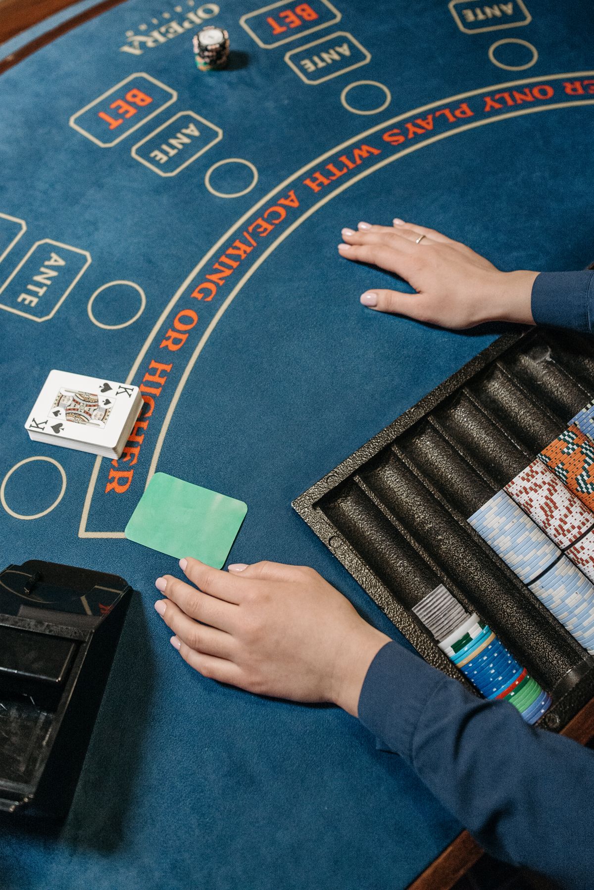 Dealer's hands and a shoe of cards on a blue baccarat table marked with player, banker and tie betting positions