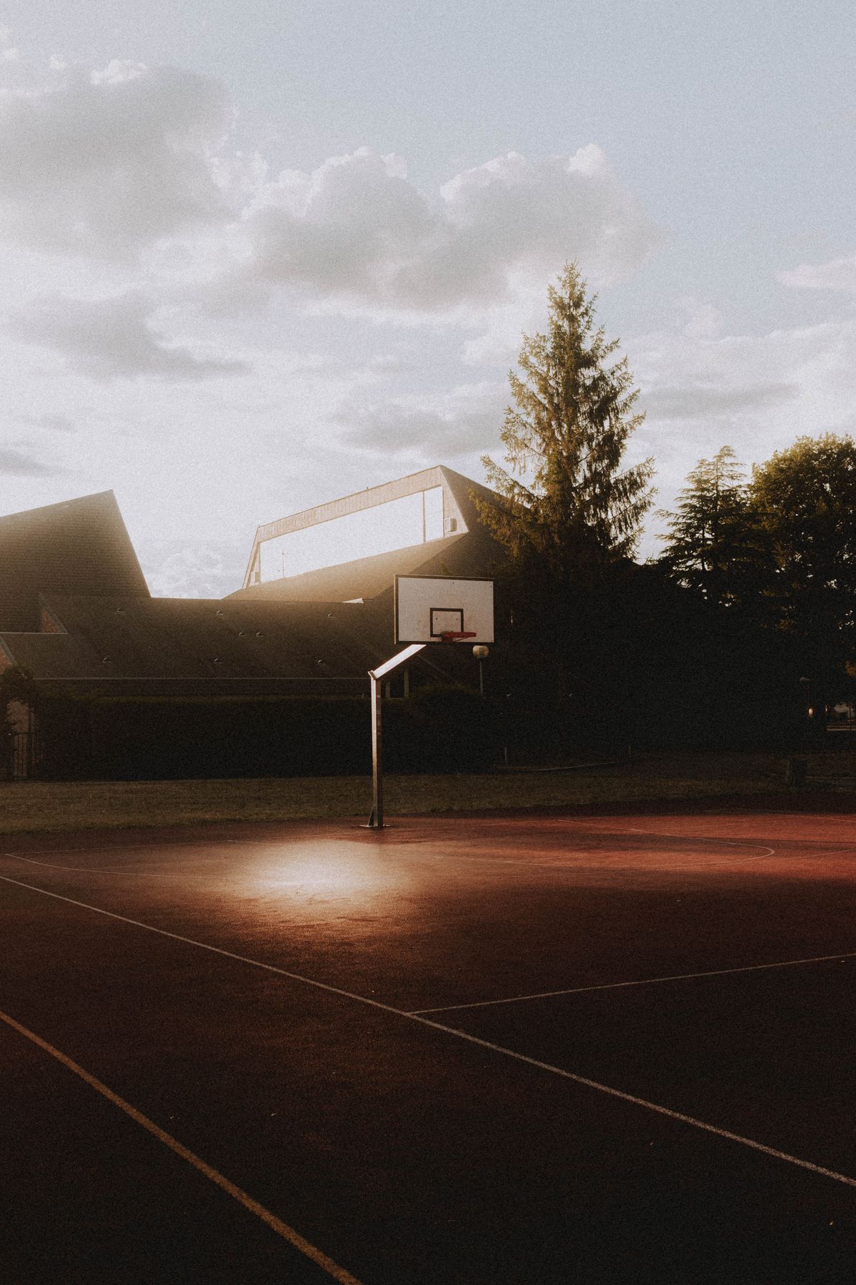 Basketball hoop on an outdoor court illuminated by a spotlight at dusk