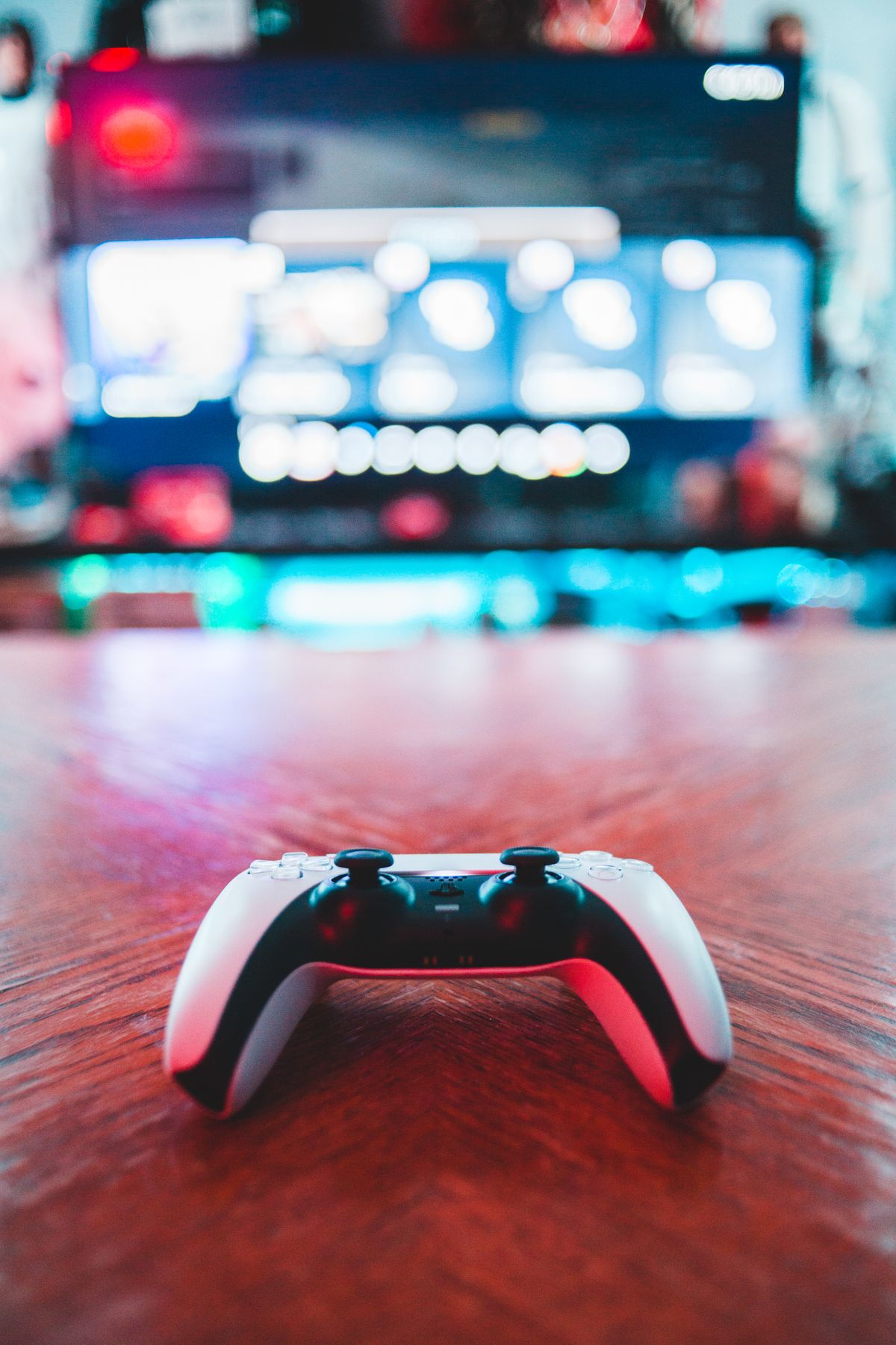 PlayStation controller on a table with a blurred gaming screen behind