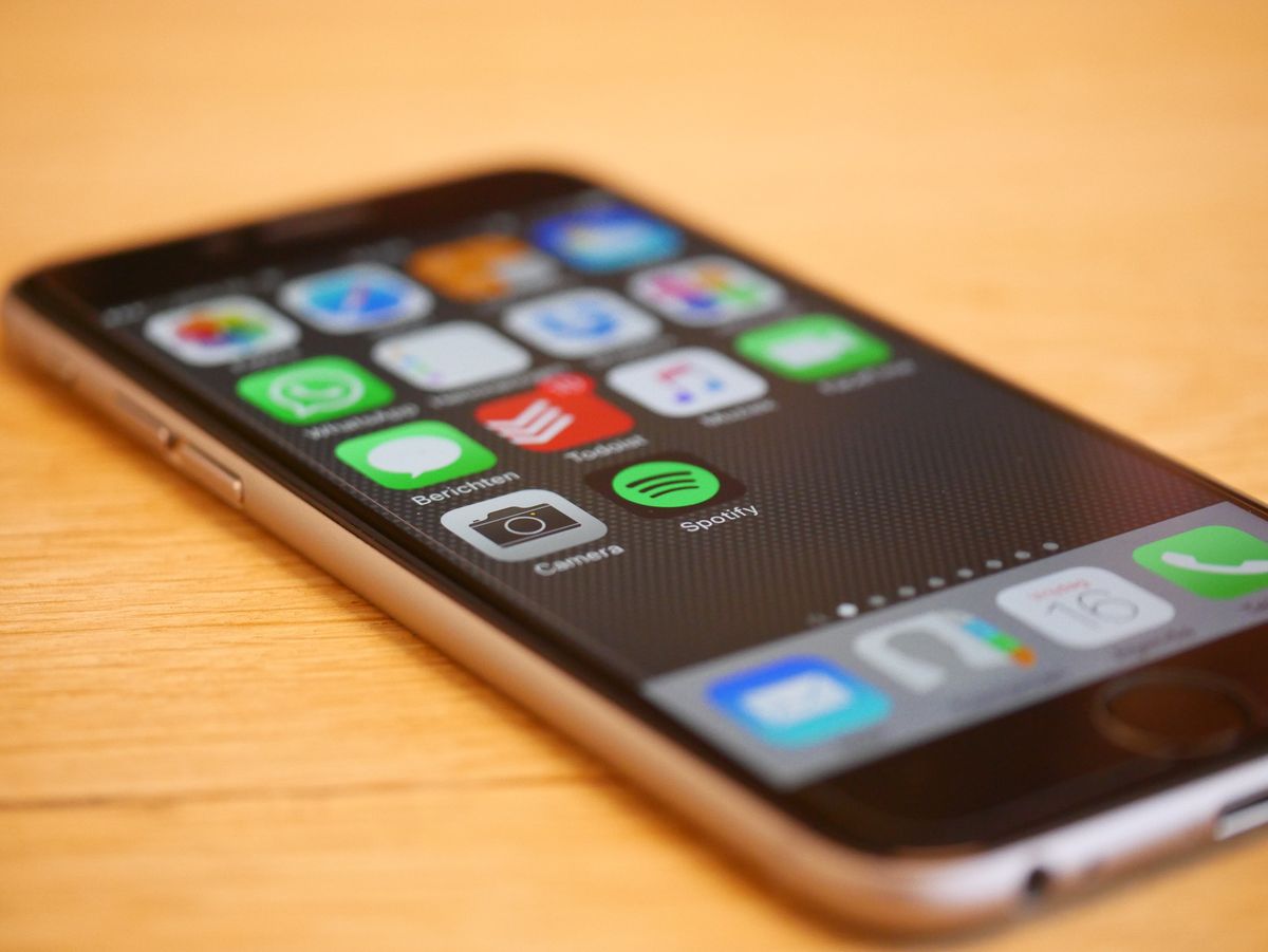 Smartphone displaying app icons on a home screen resting on a wooden surface