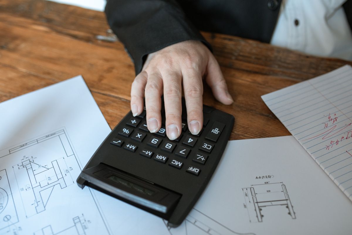 Hand operating a calculator on a wooden desk with notes