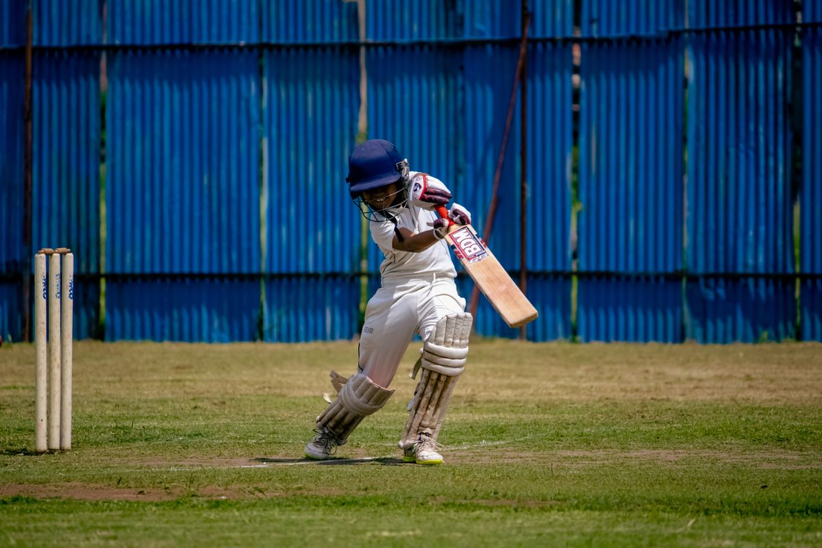 Cricket batsman in white gear and blue helmet batting on a grassy field