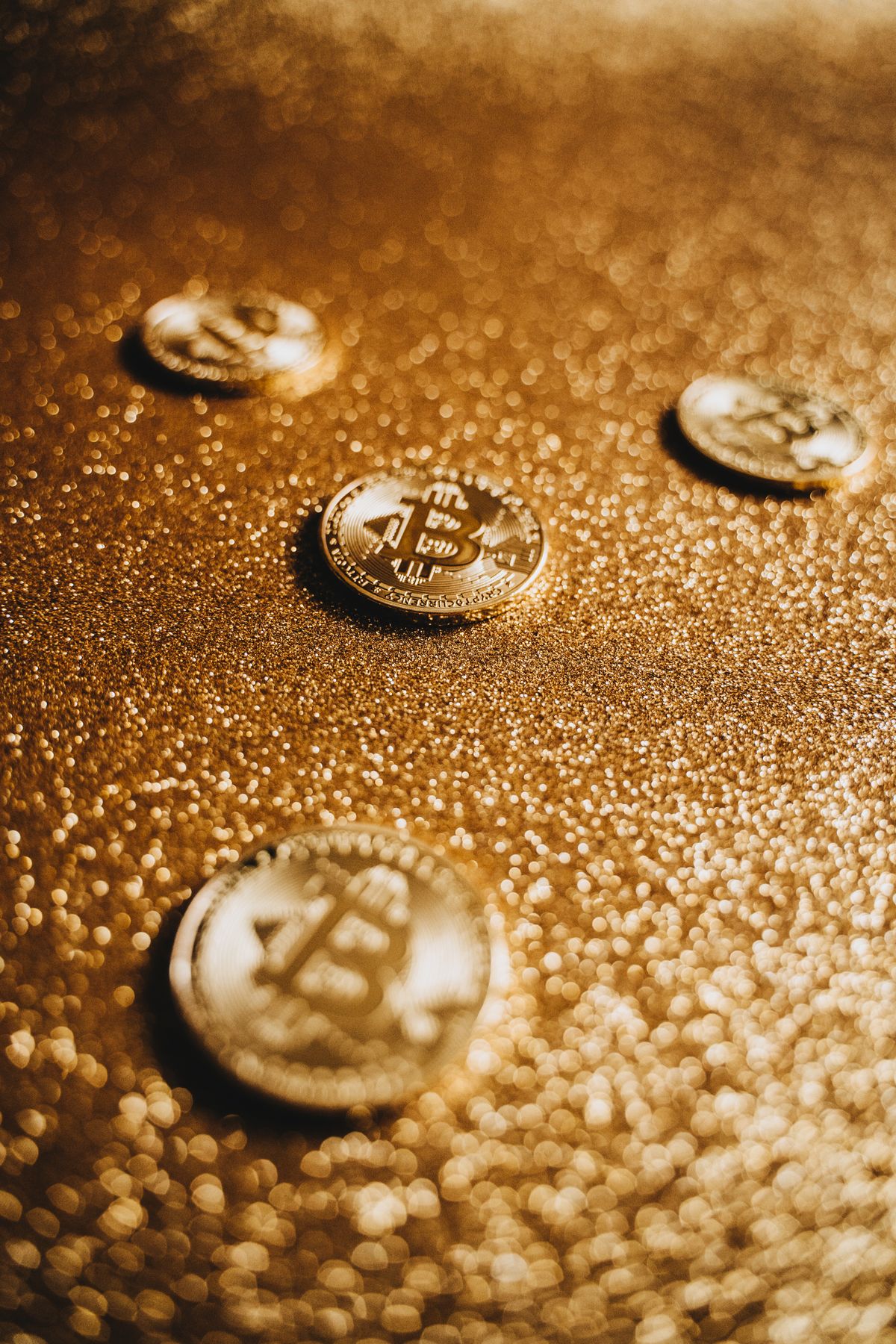 Four physical Bitcoin coins scattered on a golden glittering surface