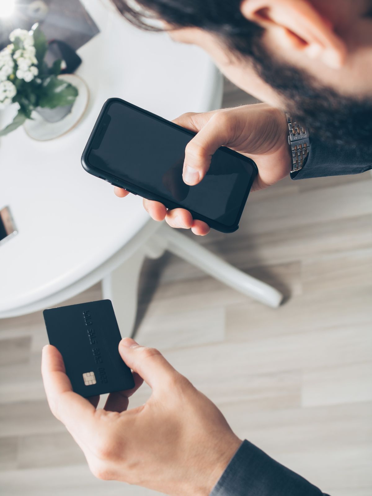 Hands holding a smartphone and a credit card over a table