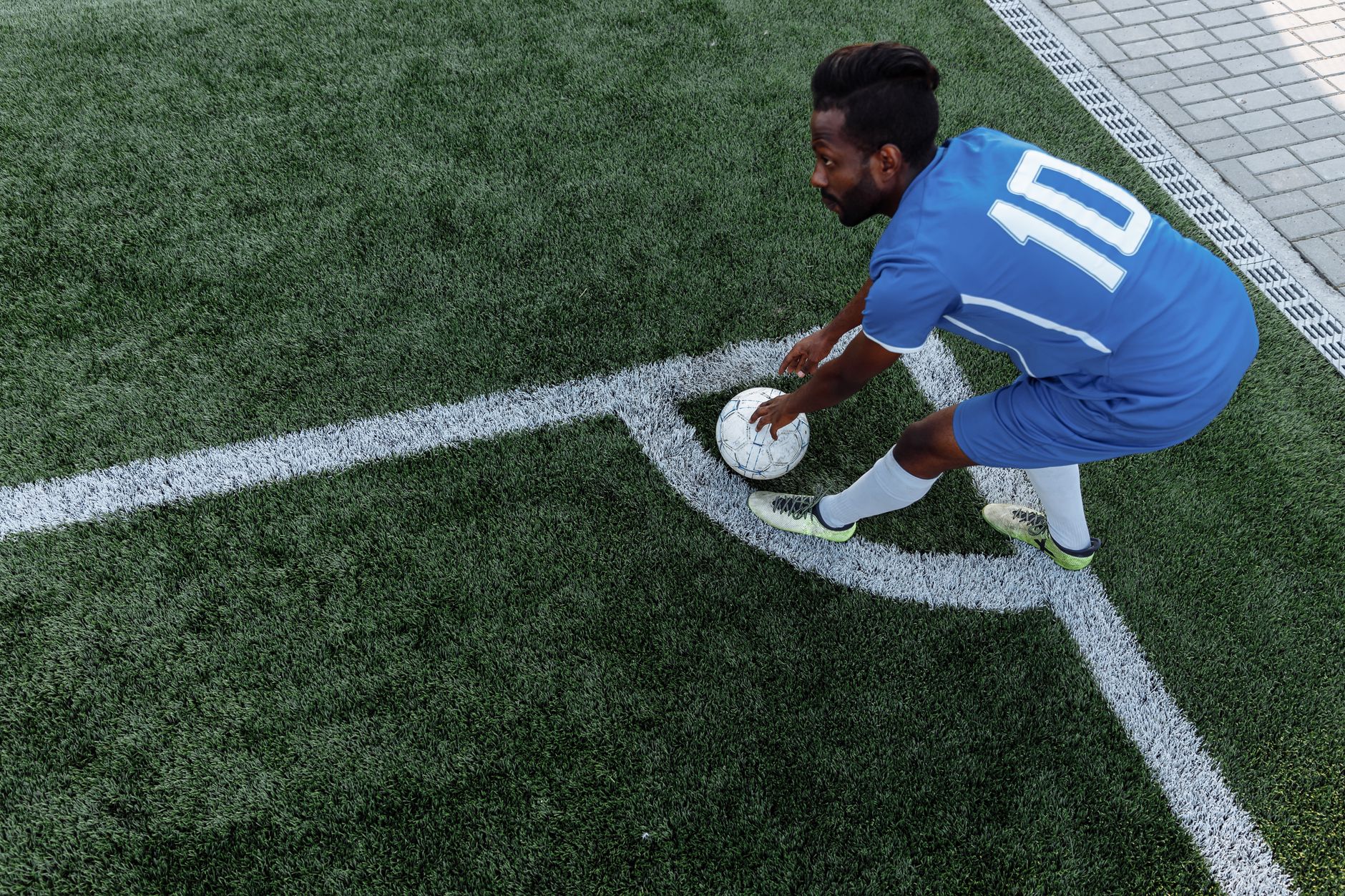 A soccer player in a blue jersey prepares to kick the ball from the corner on an artificial turf field