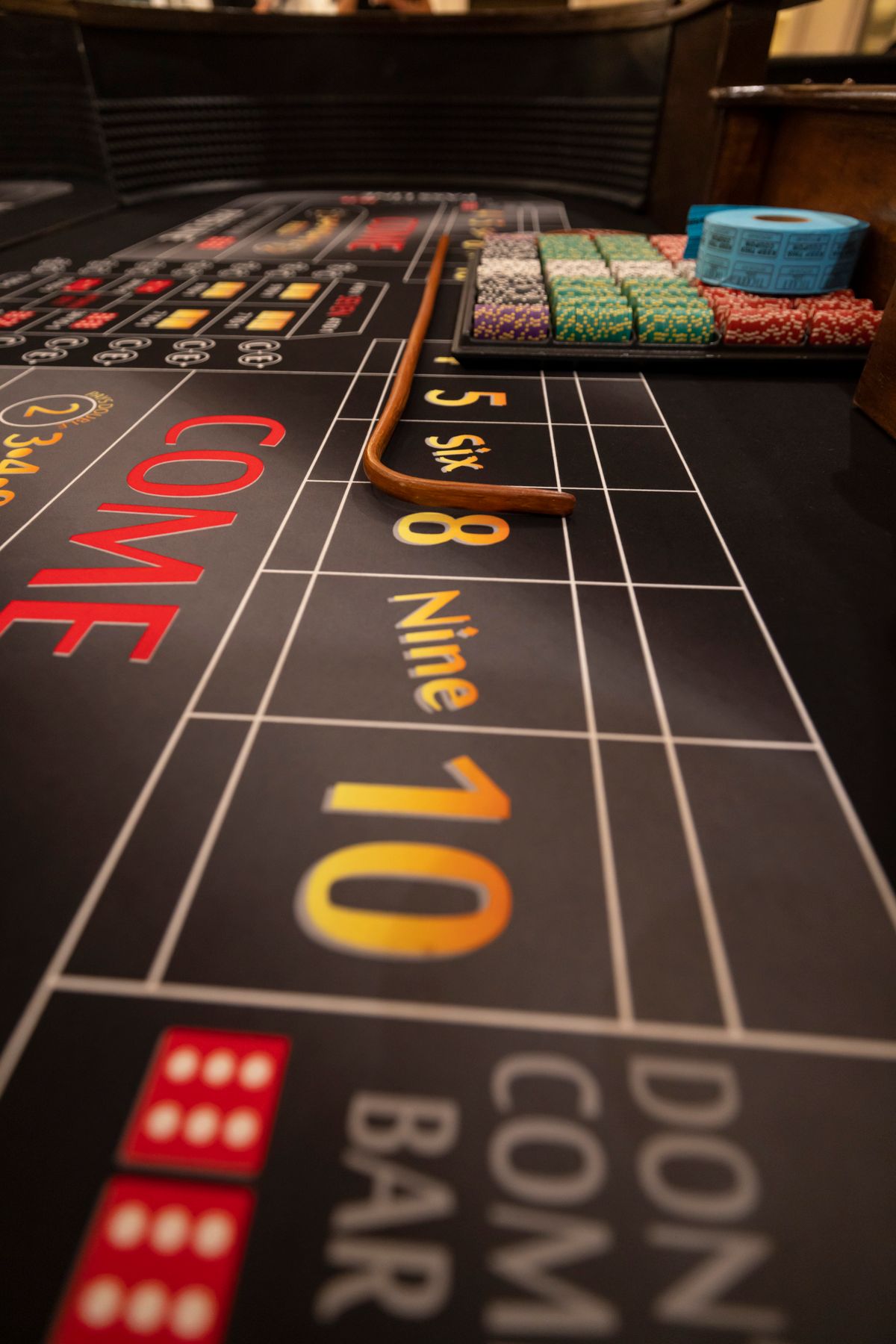 A craps table showing betting numbers, the pass line, a dice rack and a dealer stick