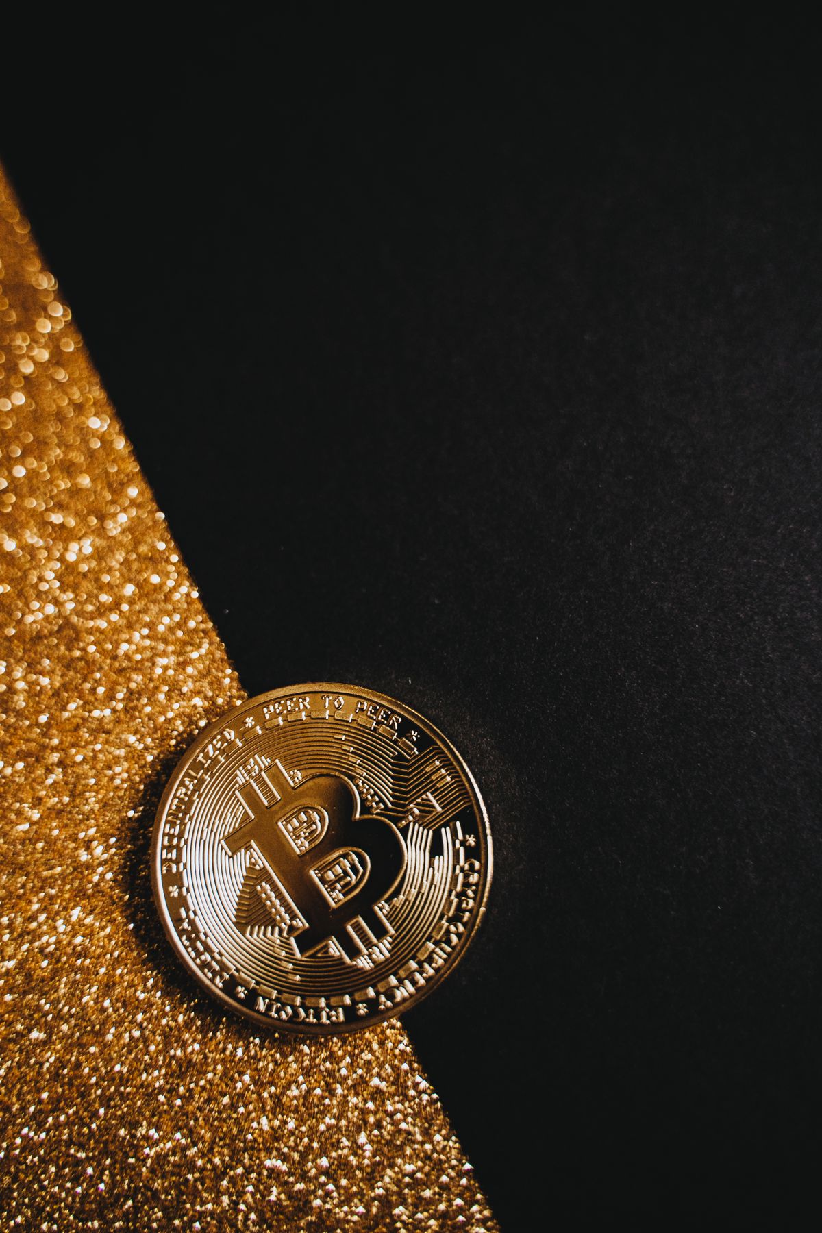 Close-up of a shiny gold Bitcoin coin on a black reflective surface