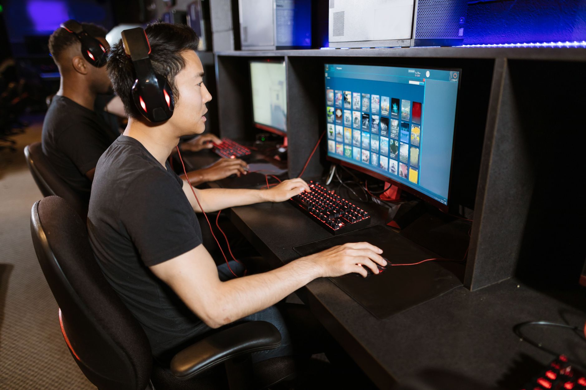Two young men play video games at a cyber cafe, showcasing modern gaming technology indoors