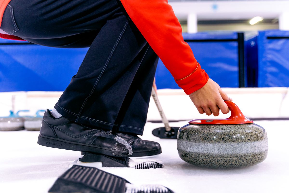 A curler holding a granite stone ready to deliver it on an indoor ice rink
