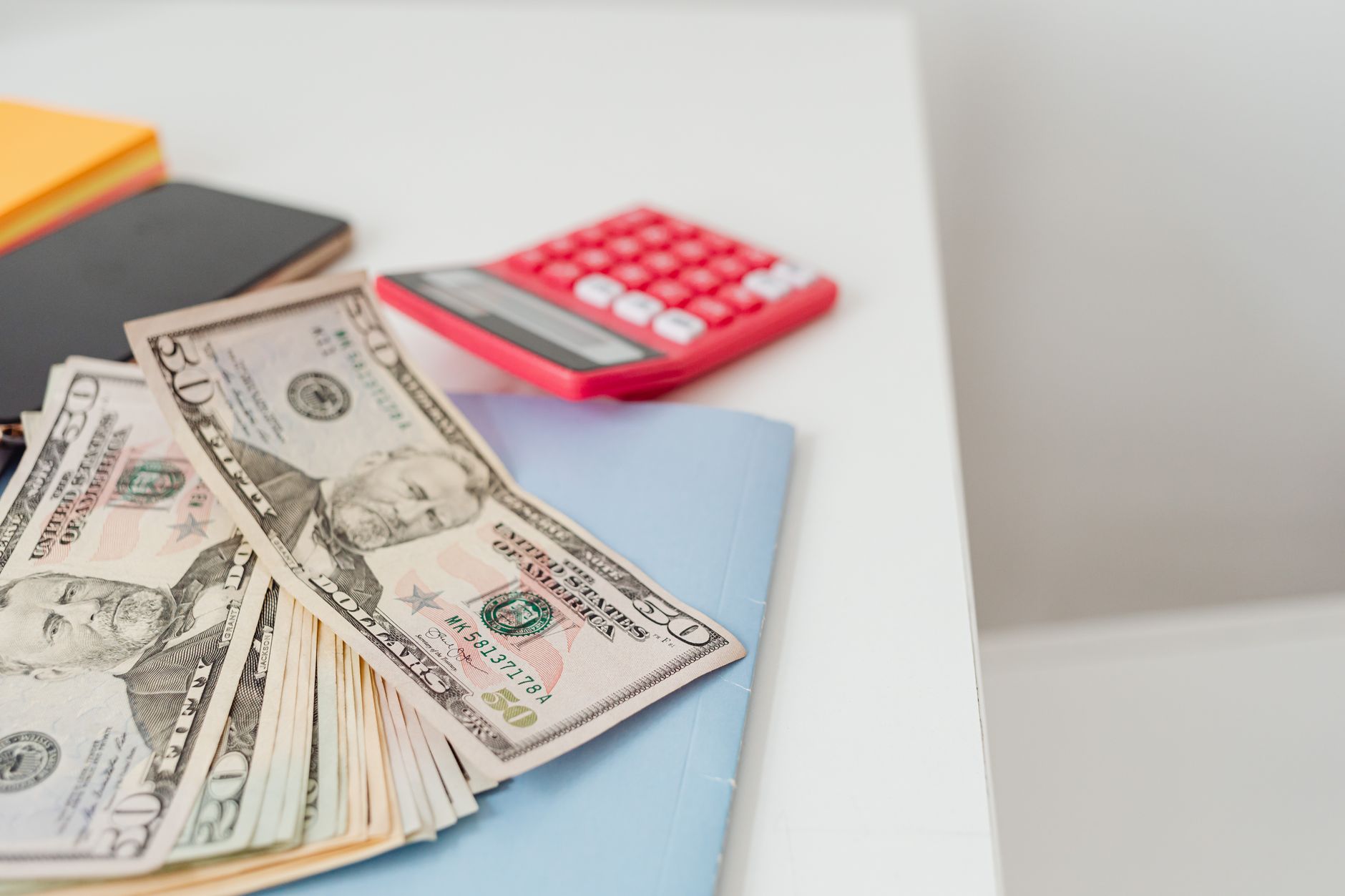 Close-up of notebooks, US dollars, and a calculator on a desk