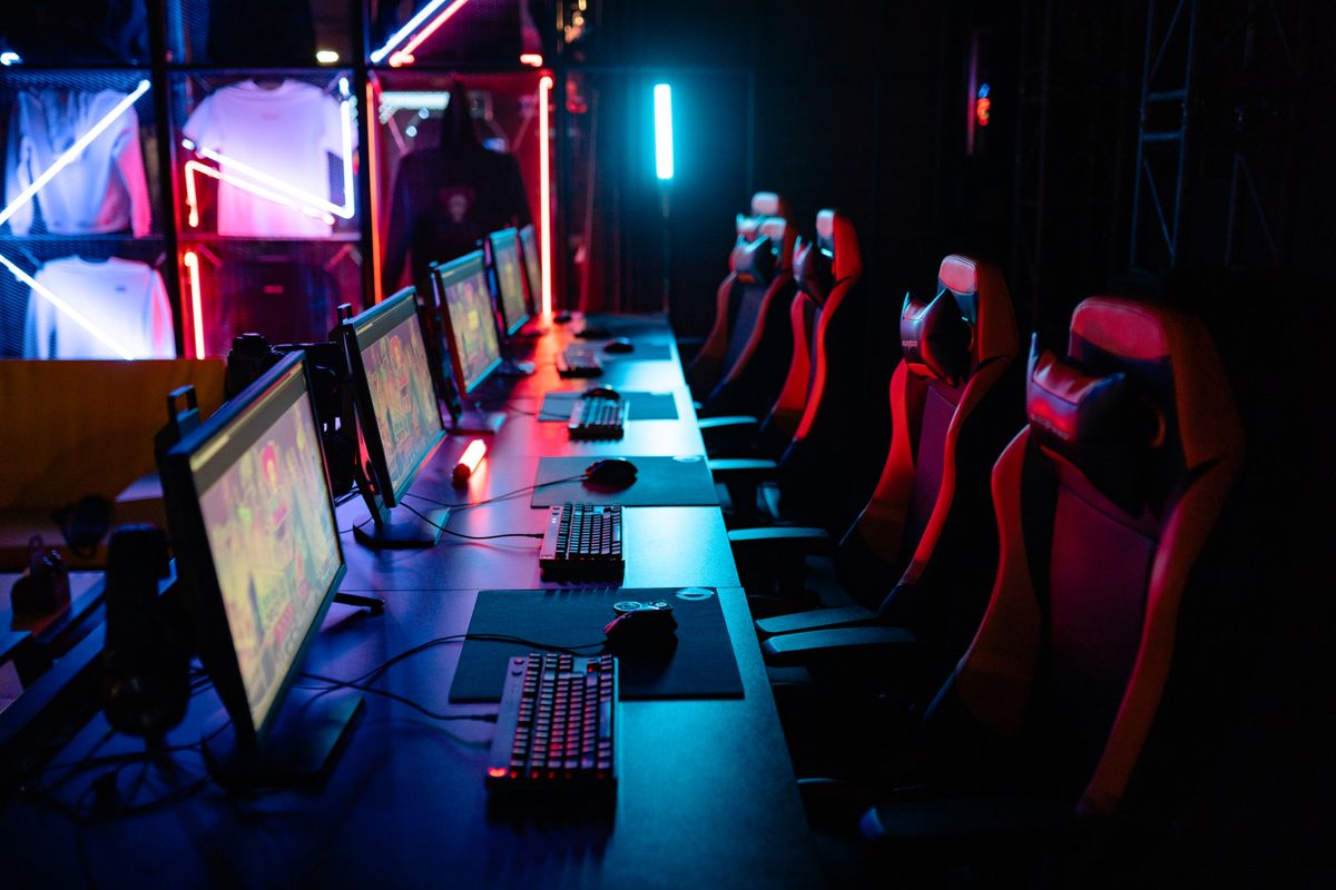 A competitive gaming room with PCs, monitors and gaming chairs lit in colour