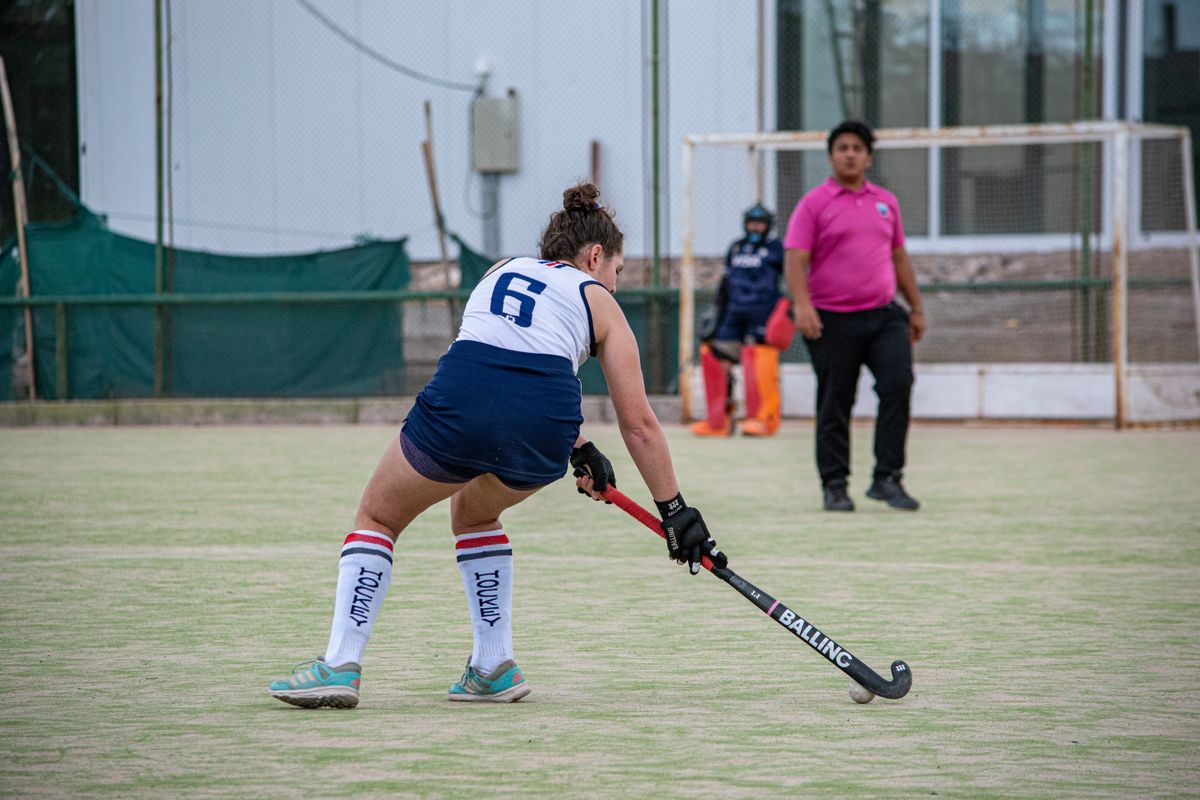 Field hockey player dribbling a yellow ball with a stick on a grass pitch
