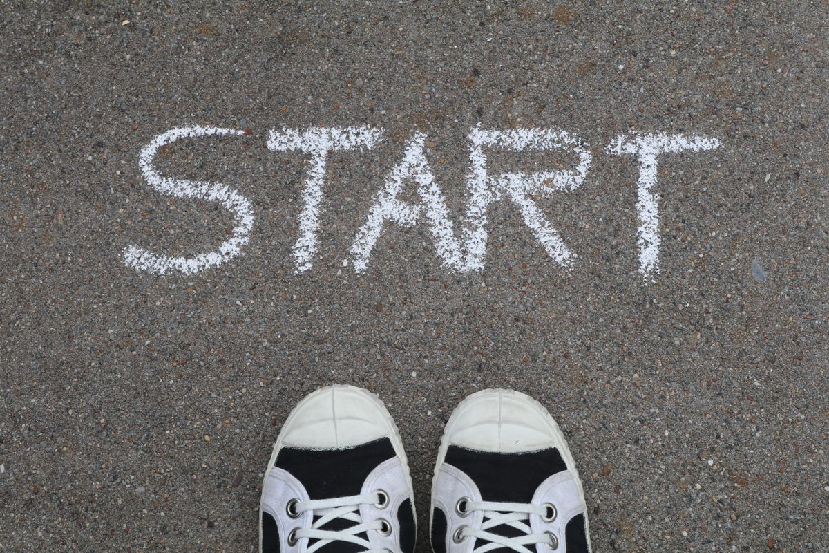 Sneakers standing on asphalt in front of the word START written in chalk