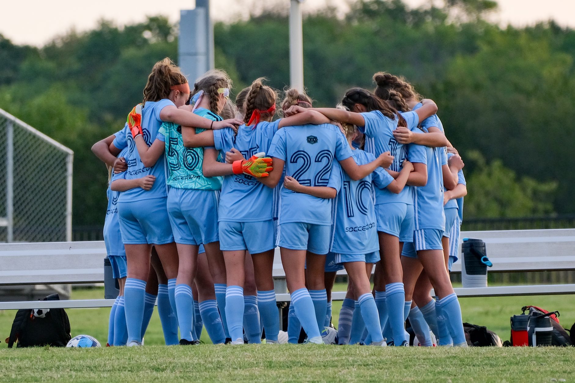 A girls' soccer team huddles together in a circle before a match, promoting teamwork and unity