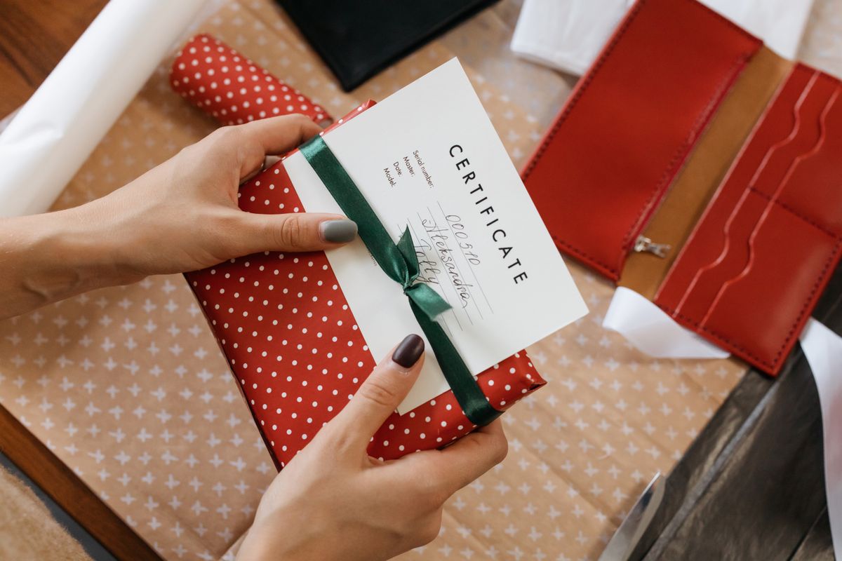 Hands holding a gift-wrapped package with a certificate card and green ribbon
