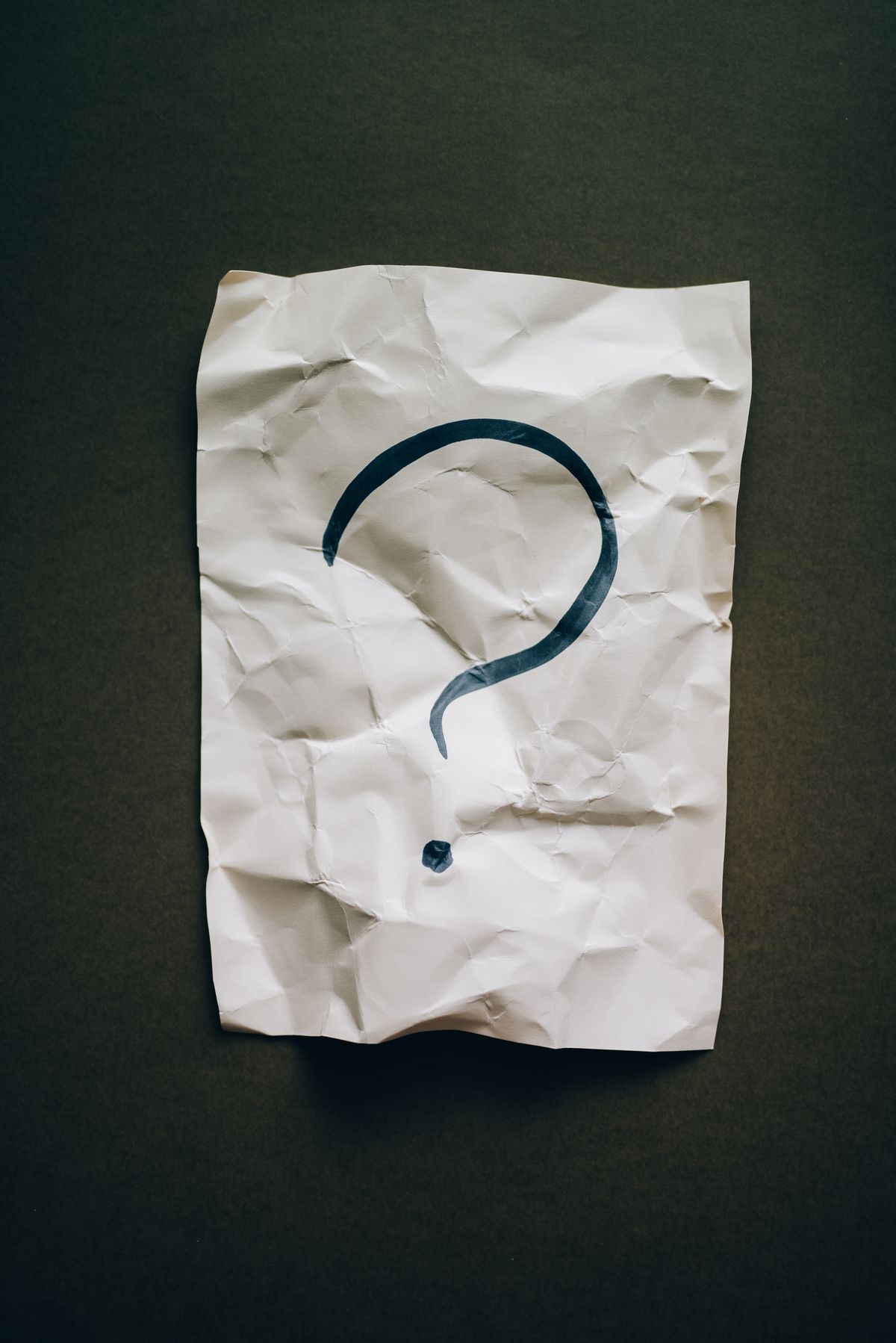 Crumpled paper with a large black question mark on a dark surface