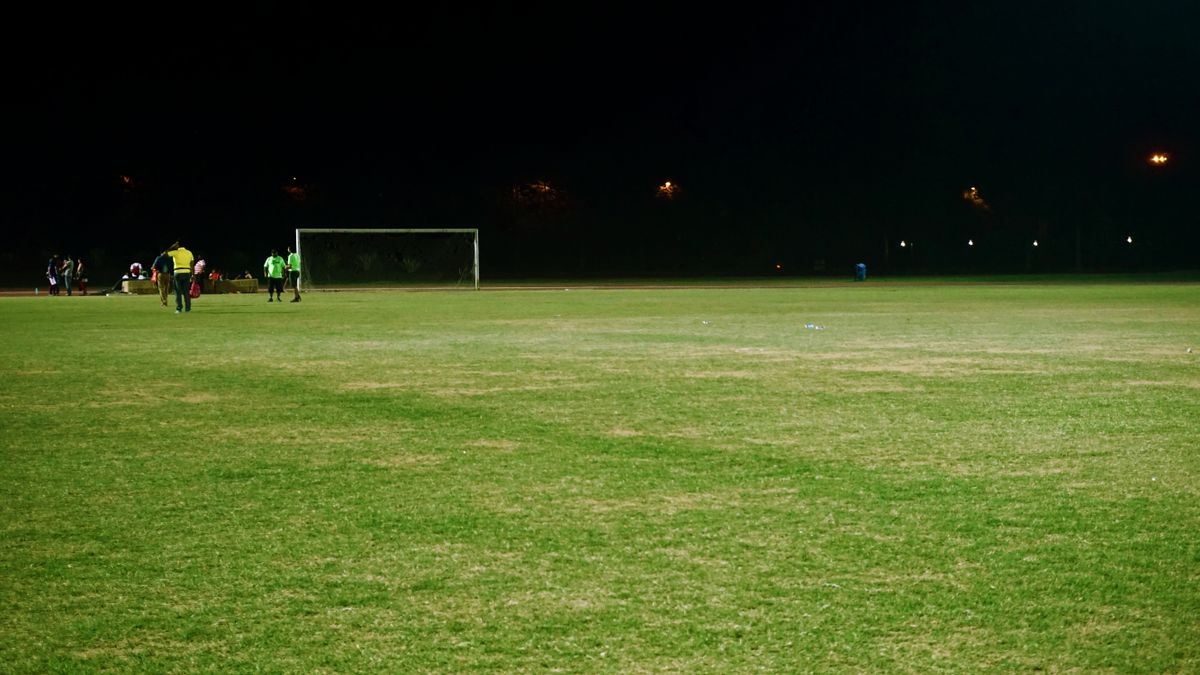 Football field illuminated by floodlights at night with players near a goal