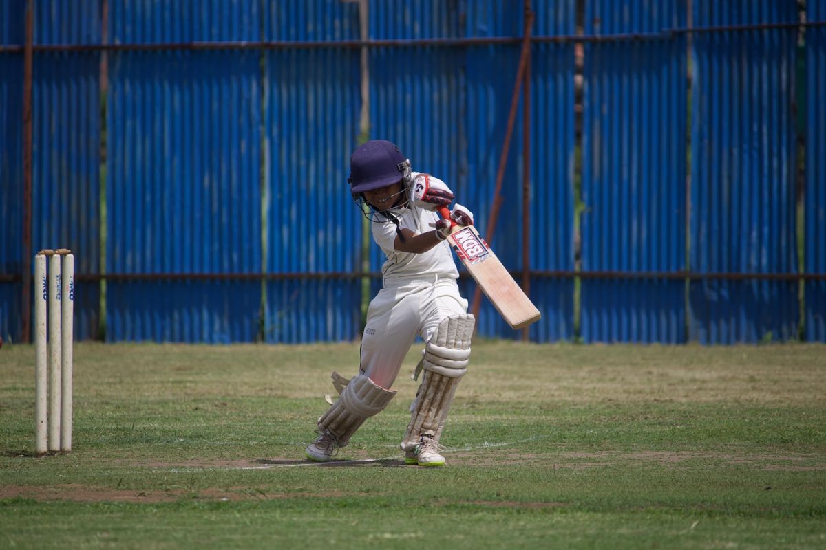 Cricket batsman in protective gear mid-swing on a grassy field