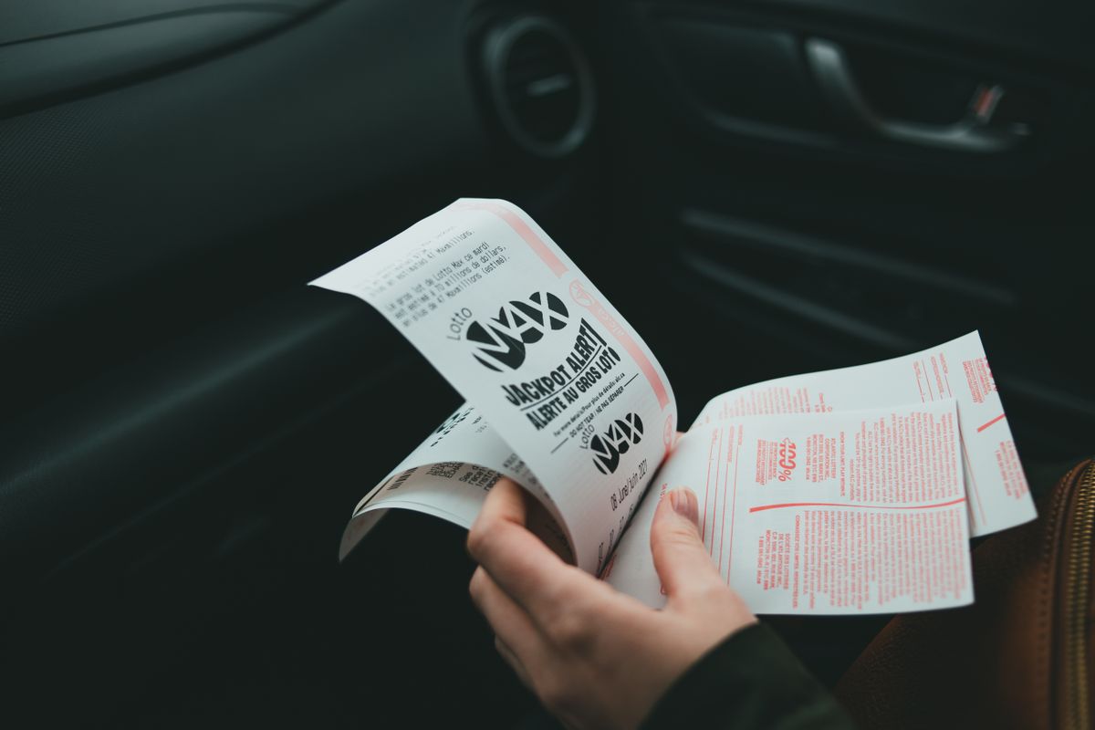 A hand holding a printed lottery ticket inside a car