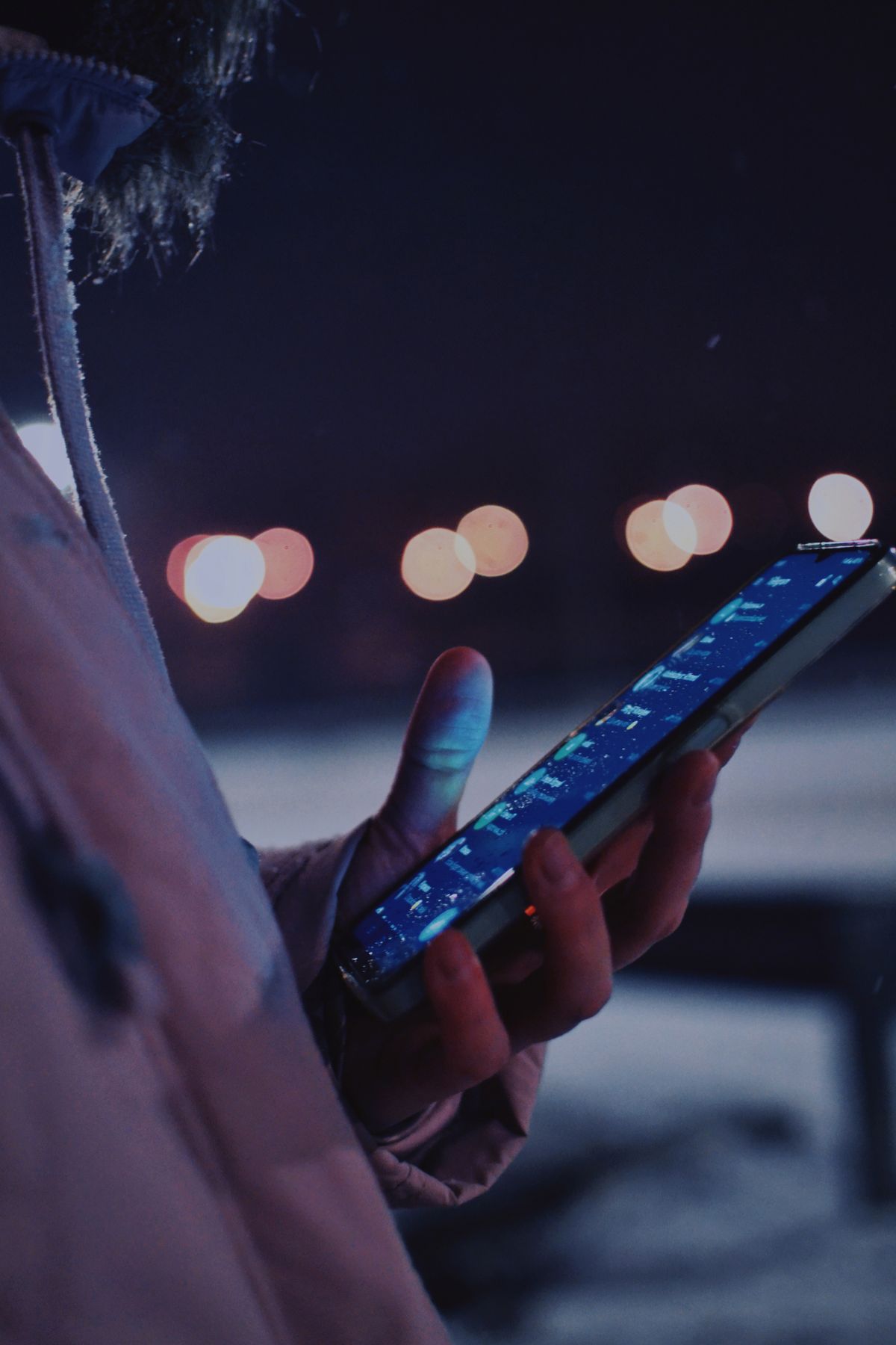 Hand holding a smartphone at night lit by city lights