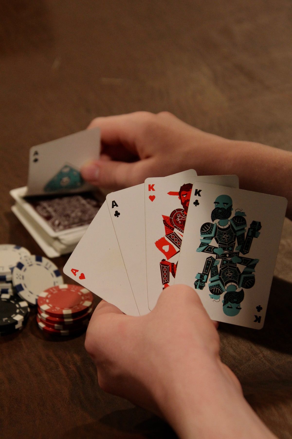 Hand holding poker cards including an ace of hearts and two kings over a wooden table