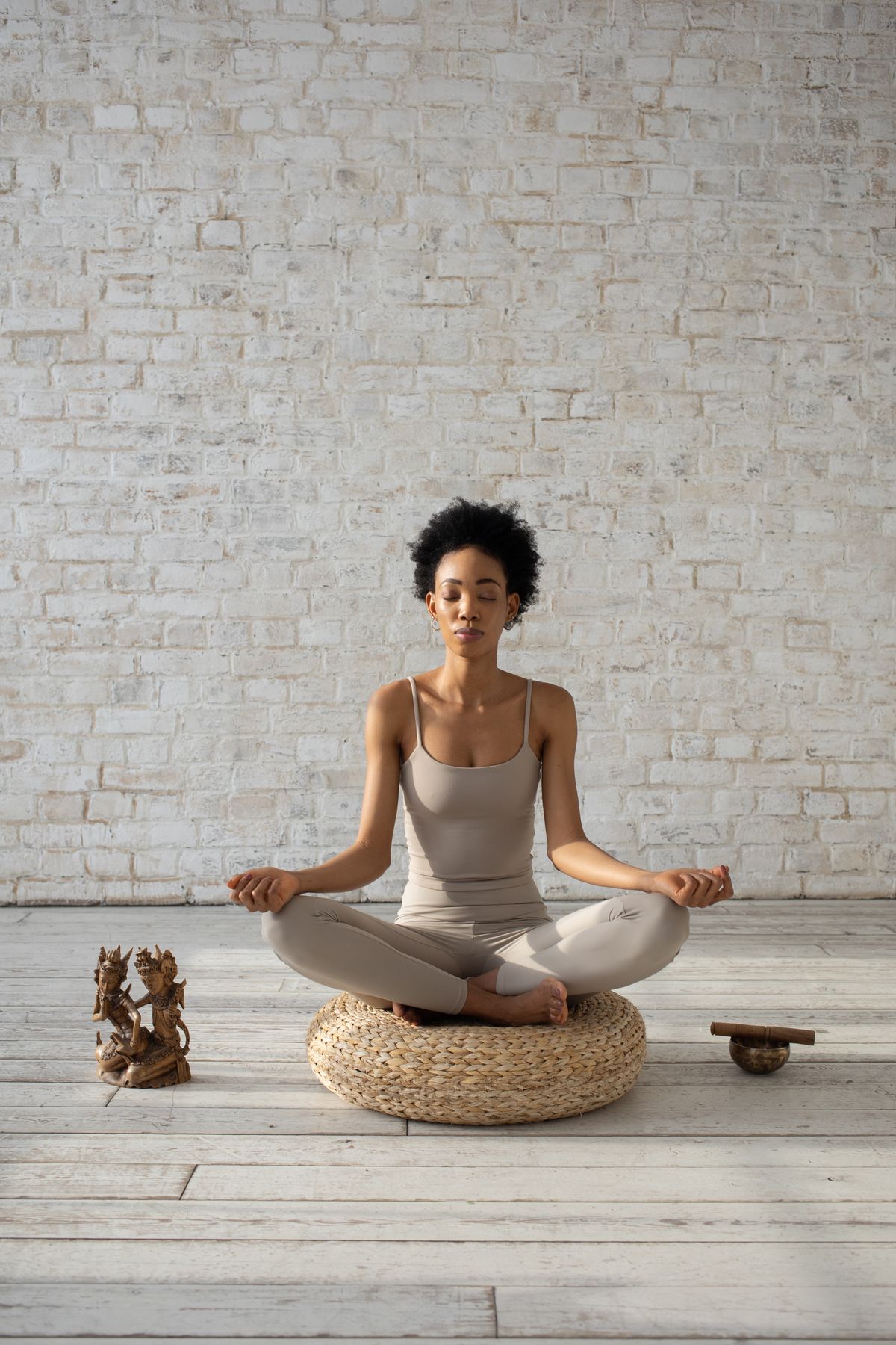 Woman meditating in a cross-legged pose on a cushion against a white brick wall