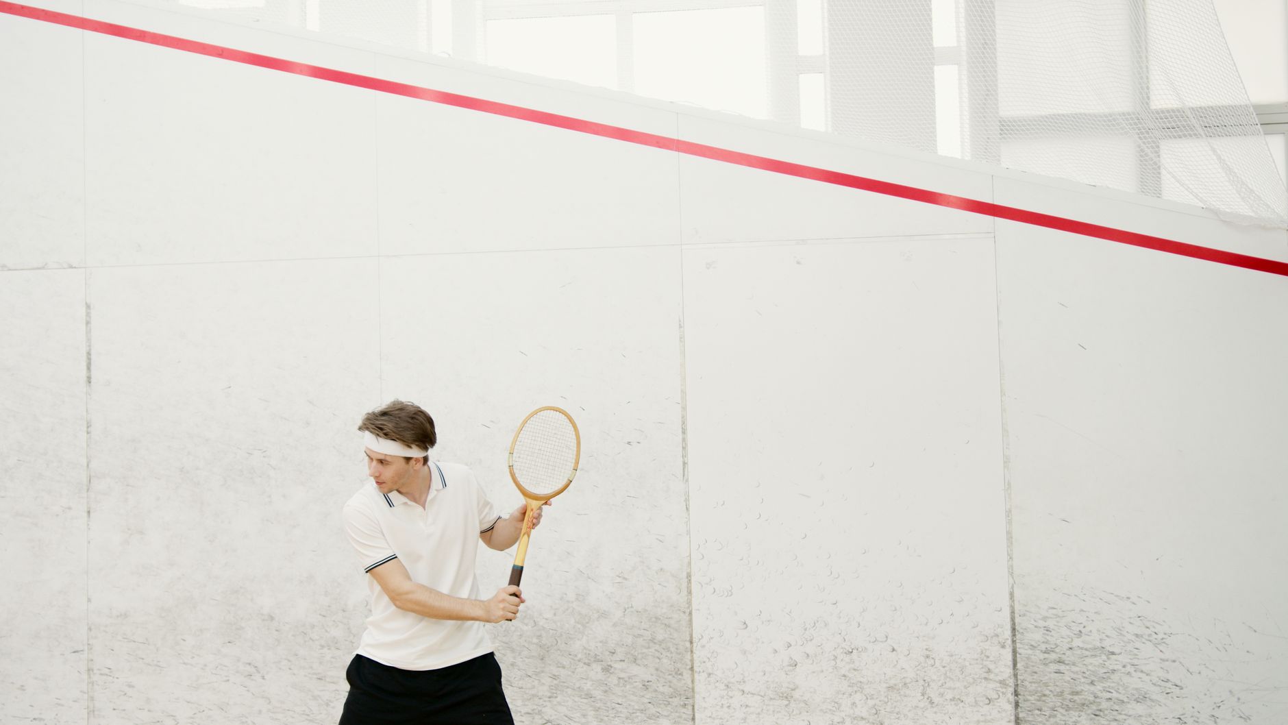 Active squash player in white sportswear preparing for a serve on indoor court
