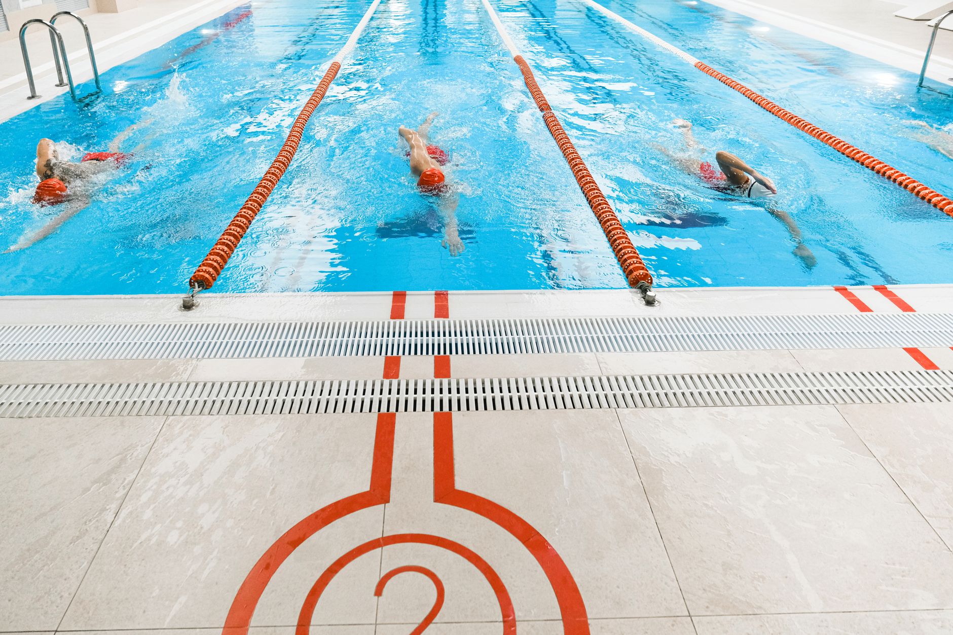 Three athletes swimming freestyle in a bright indoor pool