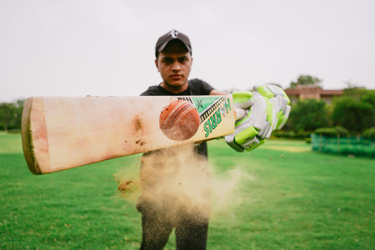 Cricketer wearing a cap and batting gloves holding a bat in a grassy field