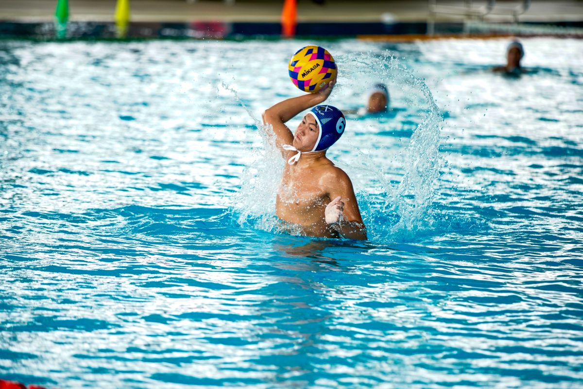 A water polo player rising out of the pool holding the ball above the water